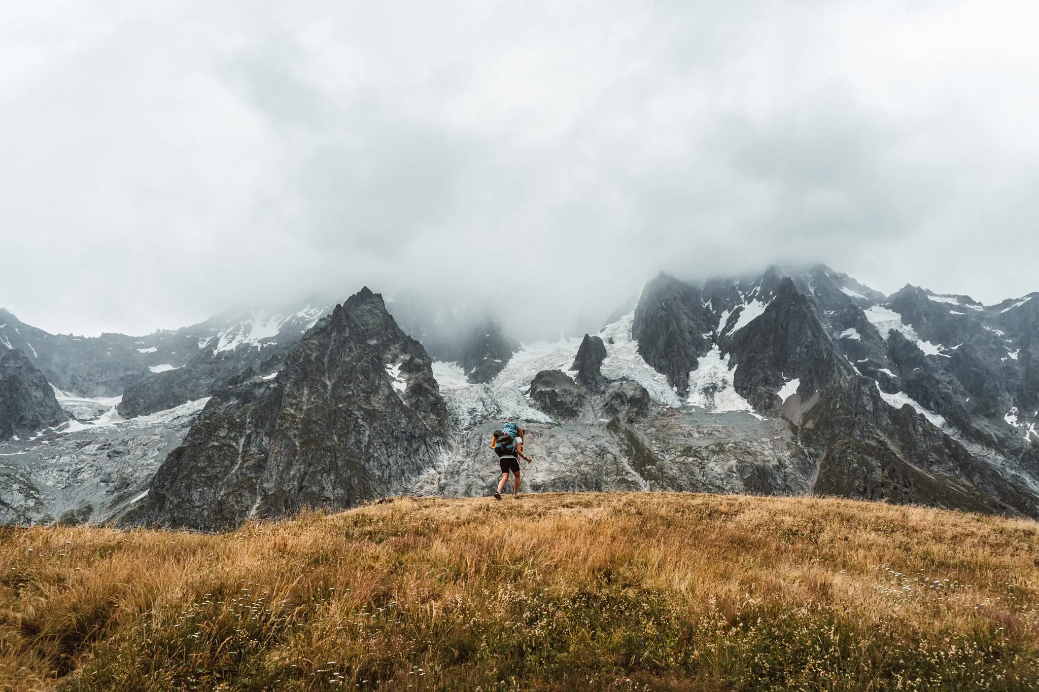 Trekař na louce pod ledovcovými štíty masivu Mont Blanc