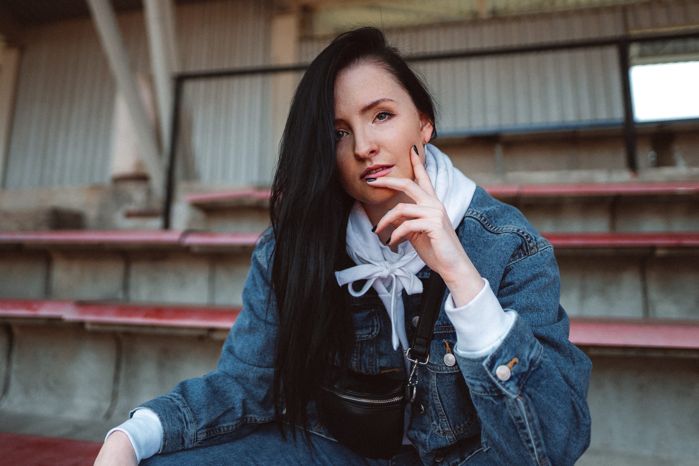 Tmavovlasá dívka v džínové bundě sedí na prázdné tribuně sportovního stadionu