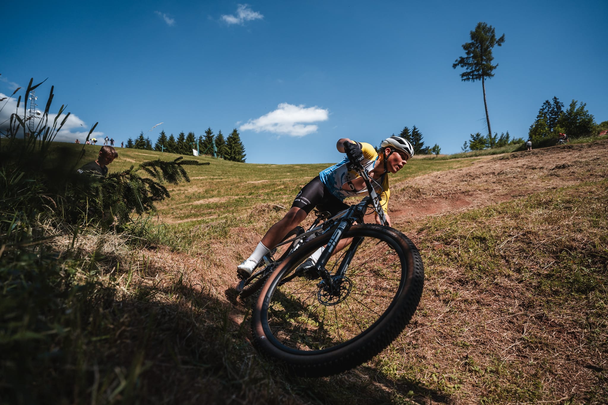 Horský cyklista se naklání do zatáčky na vyprahlé louce pod sytě modrou oblohou