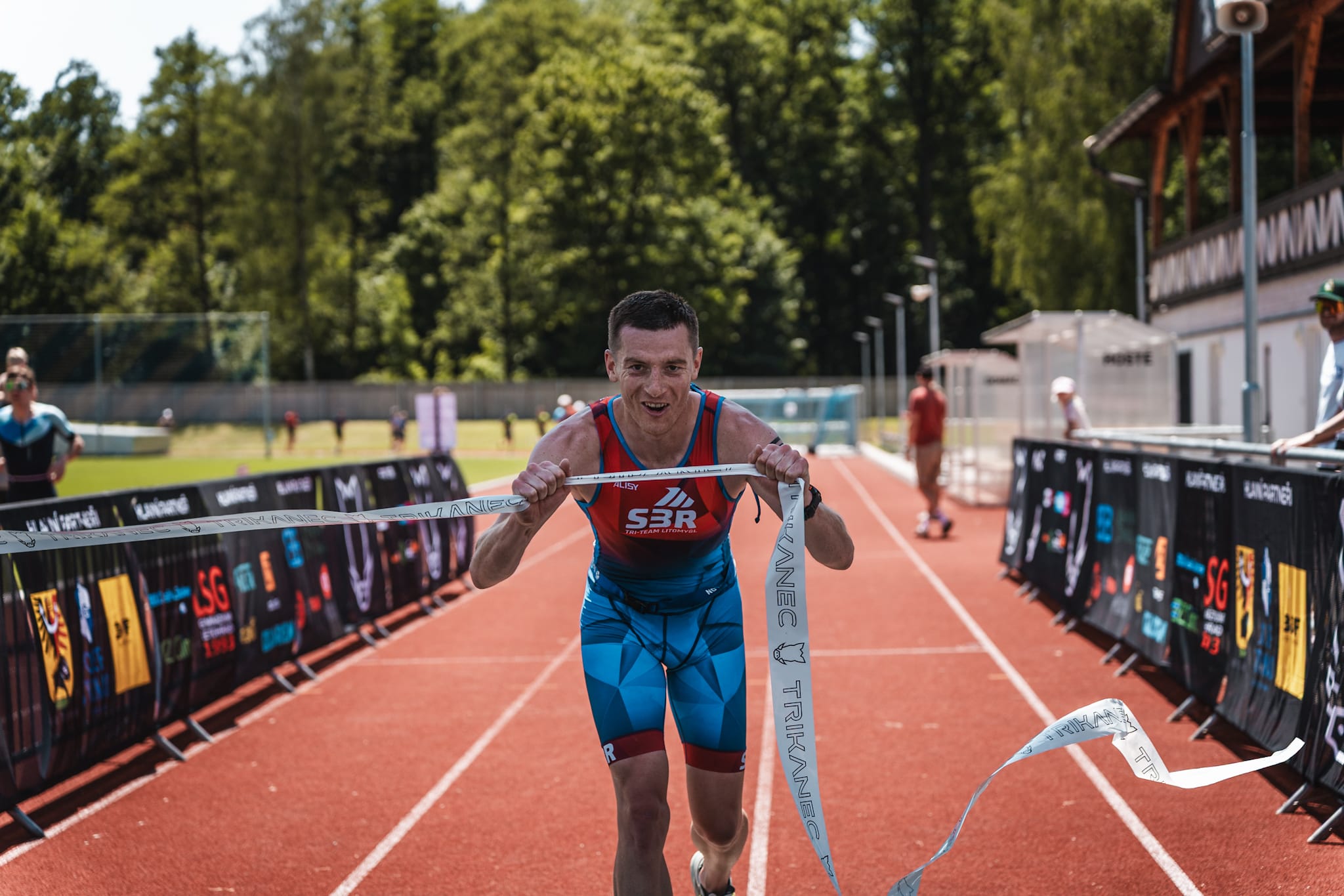 Vítěz triatlonu Trikanec protrhává cílovou pásku na atletické dráze