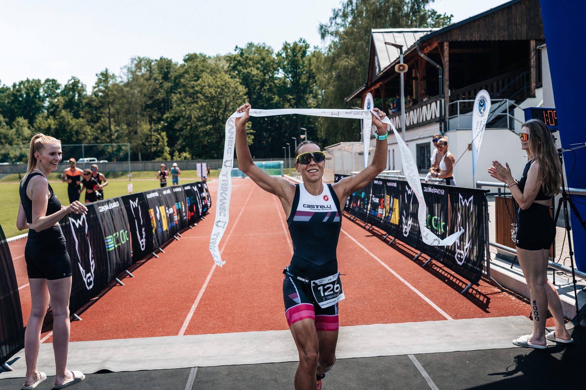 Vítězka protrhává cílovou pásku se zdviženýma rukama za potlesku pořadatelek